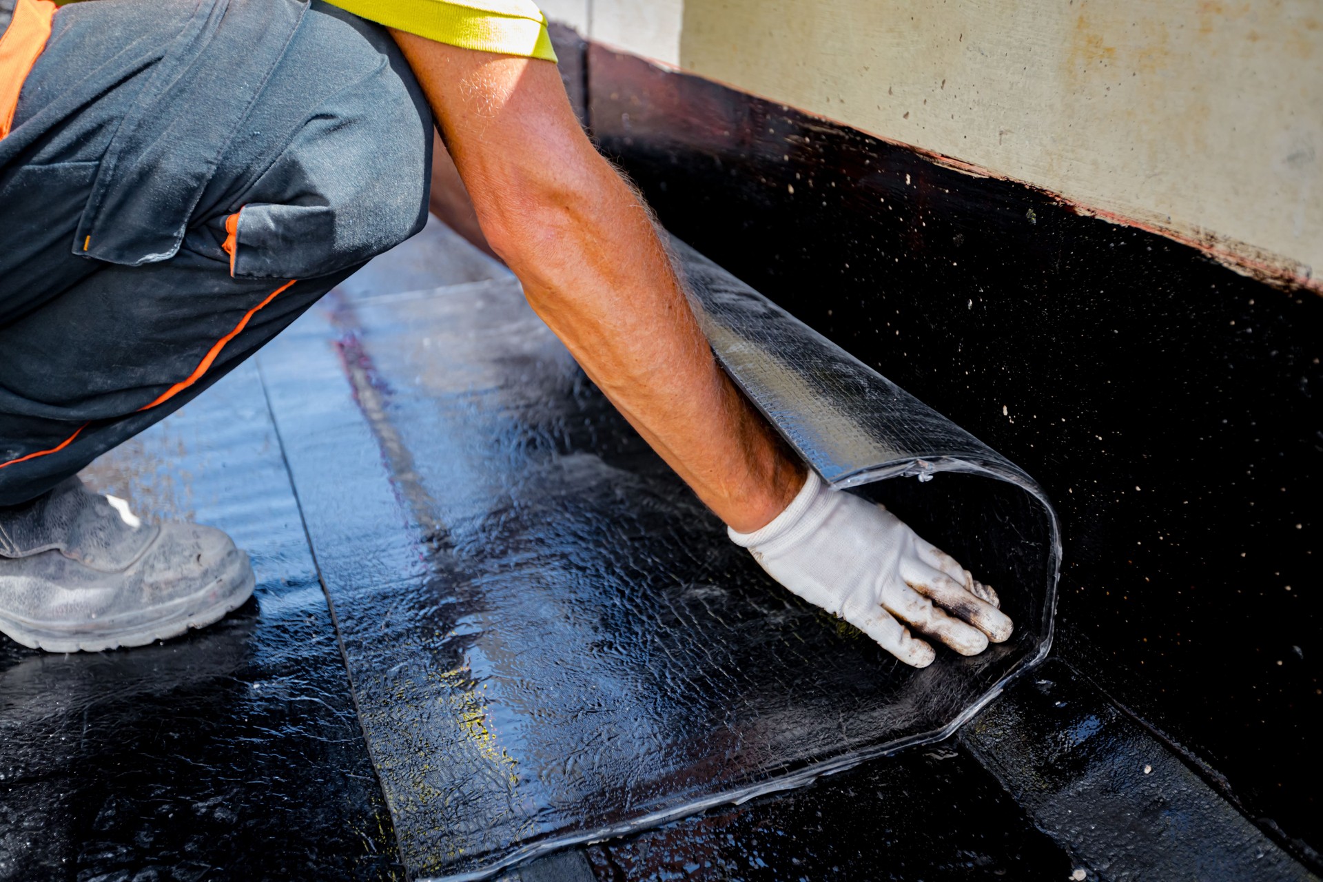 Worker unroll foil with bitumen waterproofing installation over concrete