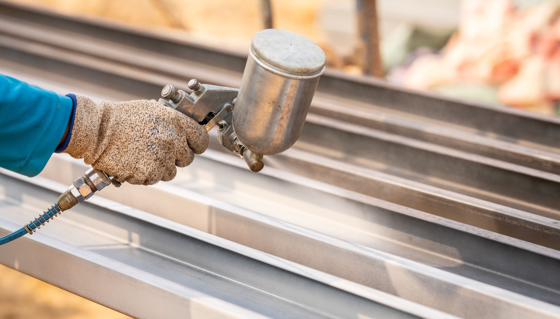 Construction worker painting metal structure surface coating with a spray gun at construction site. Metal corrosion and rust protection. Industrial precision. Protective coating to a metal structure.